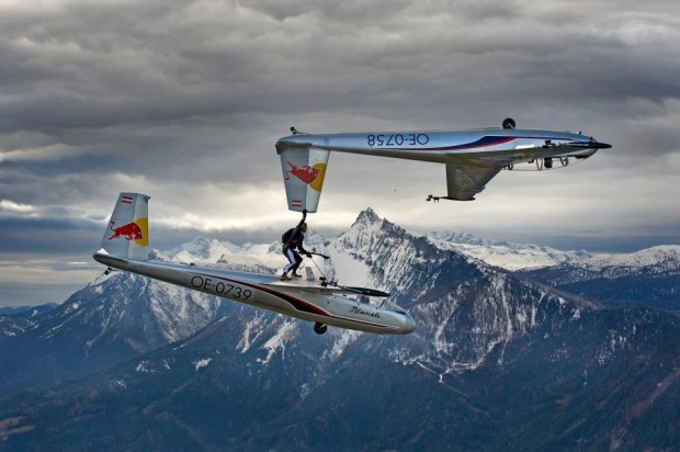 Skydiver stands on top of one plane while holding the tail of another